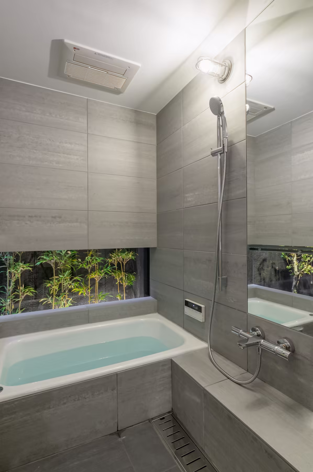 The bathroom — a deep tub and walk-in shower in pale stone tile, with a low window onto the bamboo outside