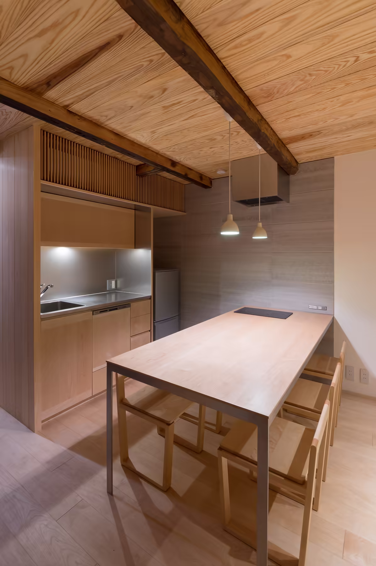 The dining table under two pendant lamps, the old blackened beam running across the ceiling above it
