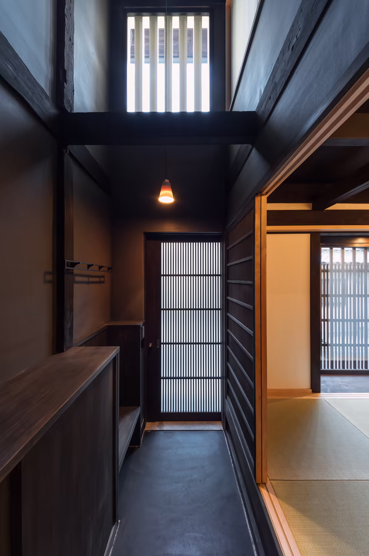 The entrance hall — blackened timber, a paper lantern, and the latticed front door onto the lane