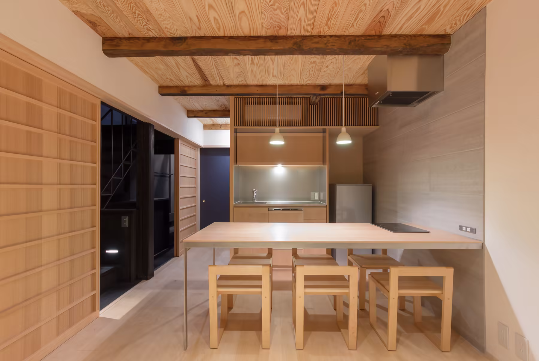 The kitchen — a stainless counter and full-height fridge set into cedar joinery, with the dining table and its stools in front