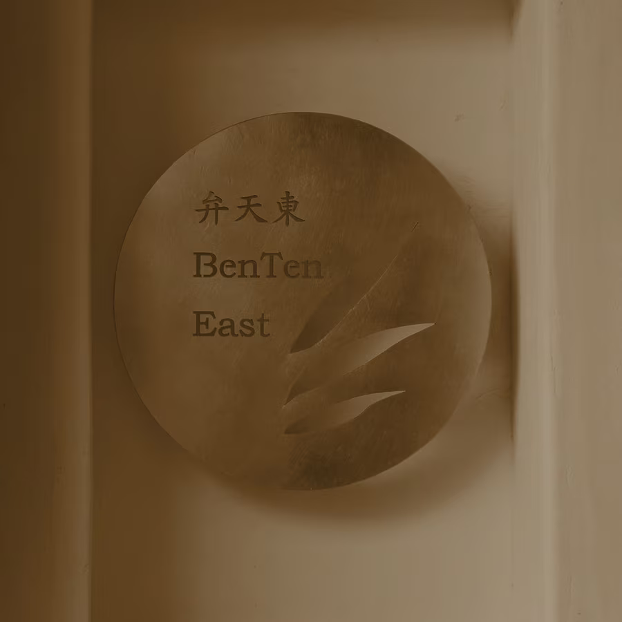 The brass name plate of BenTen East, 弁天東, set in a lit wall recess by the door