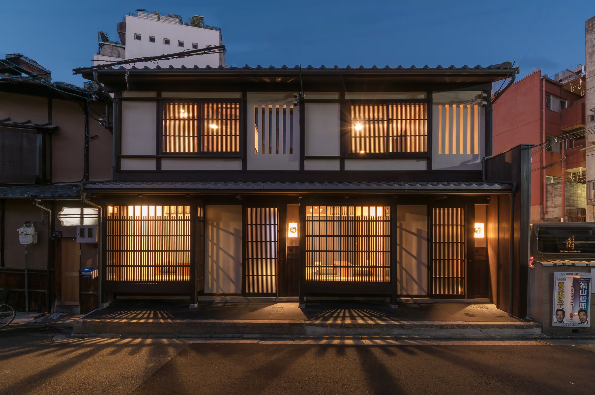 The two restored BenTen machiya at dusk, their lattice fronts lit from within, seen from the lane in Higashiyama, Kyoto