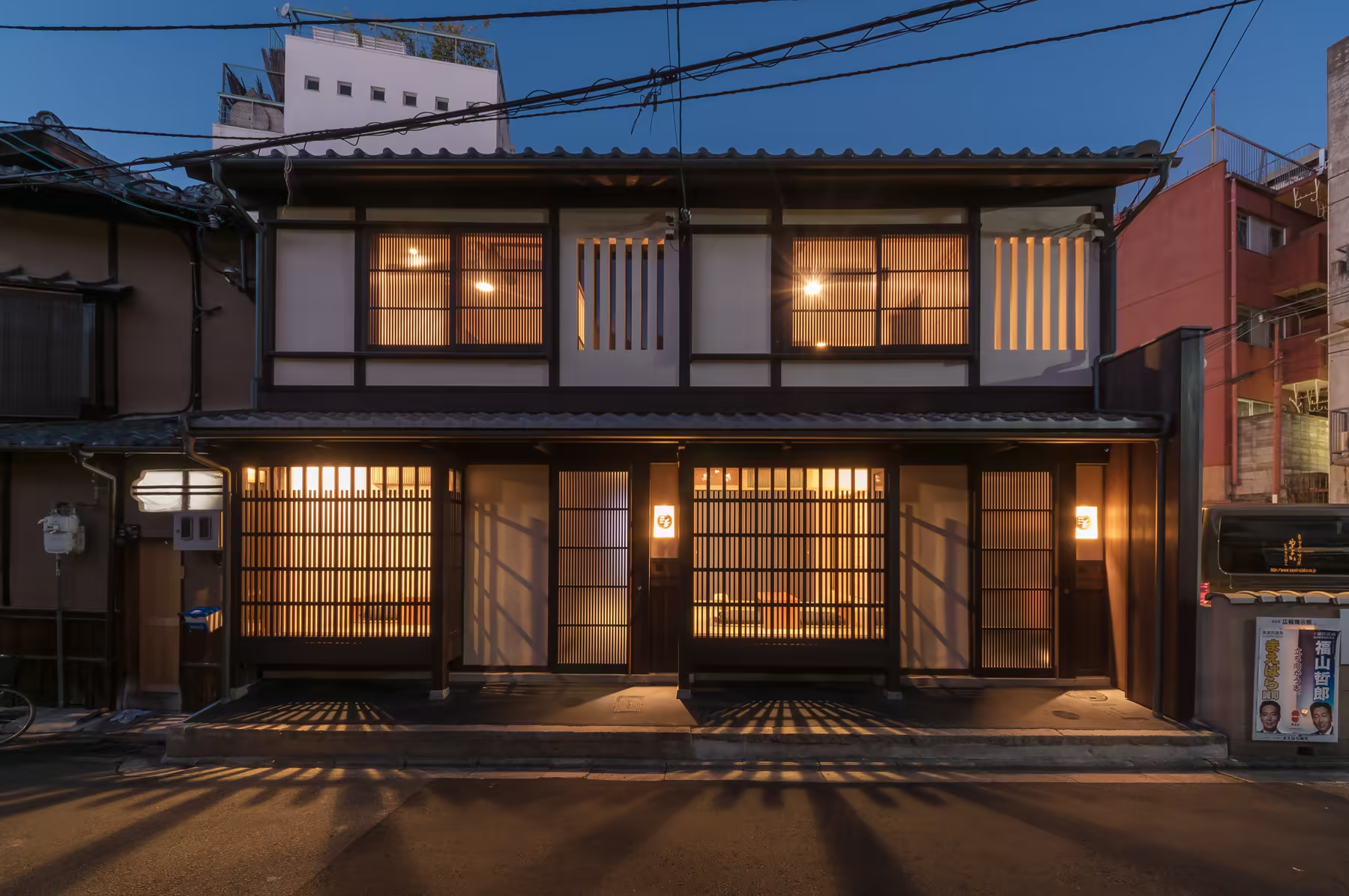 Both houses from the lane at dusk — BenTen East on the left, West alongside it, lit behind their lattice fronts