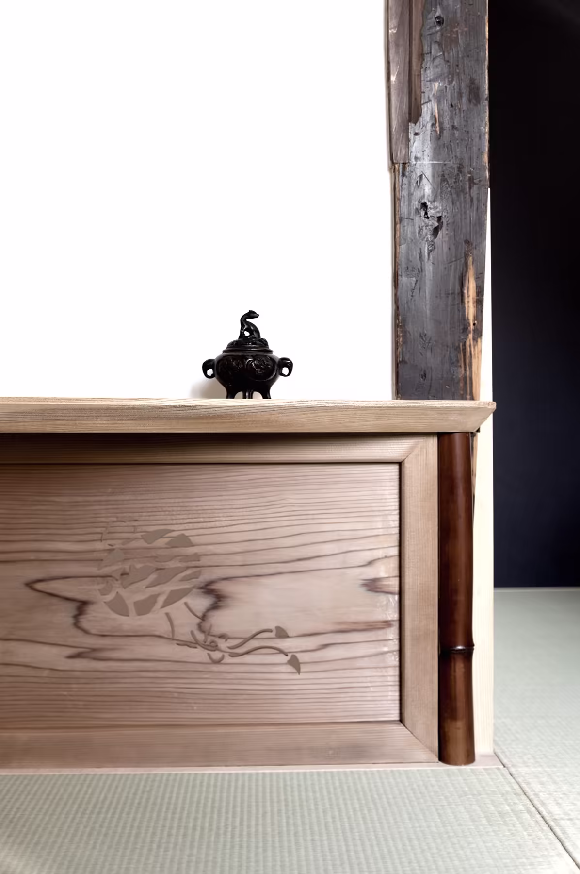 A wooden chest against a blackened post, set on the tatami