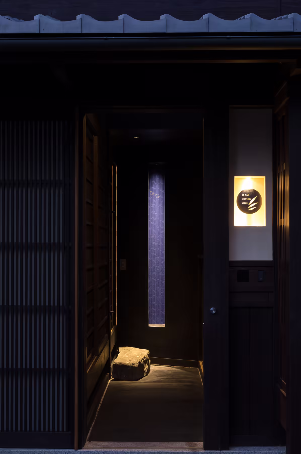 The front of BenTen West after dark, the house crest lit beside the latticed door