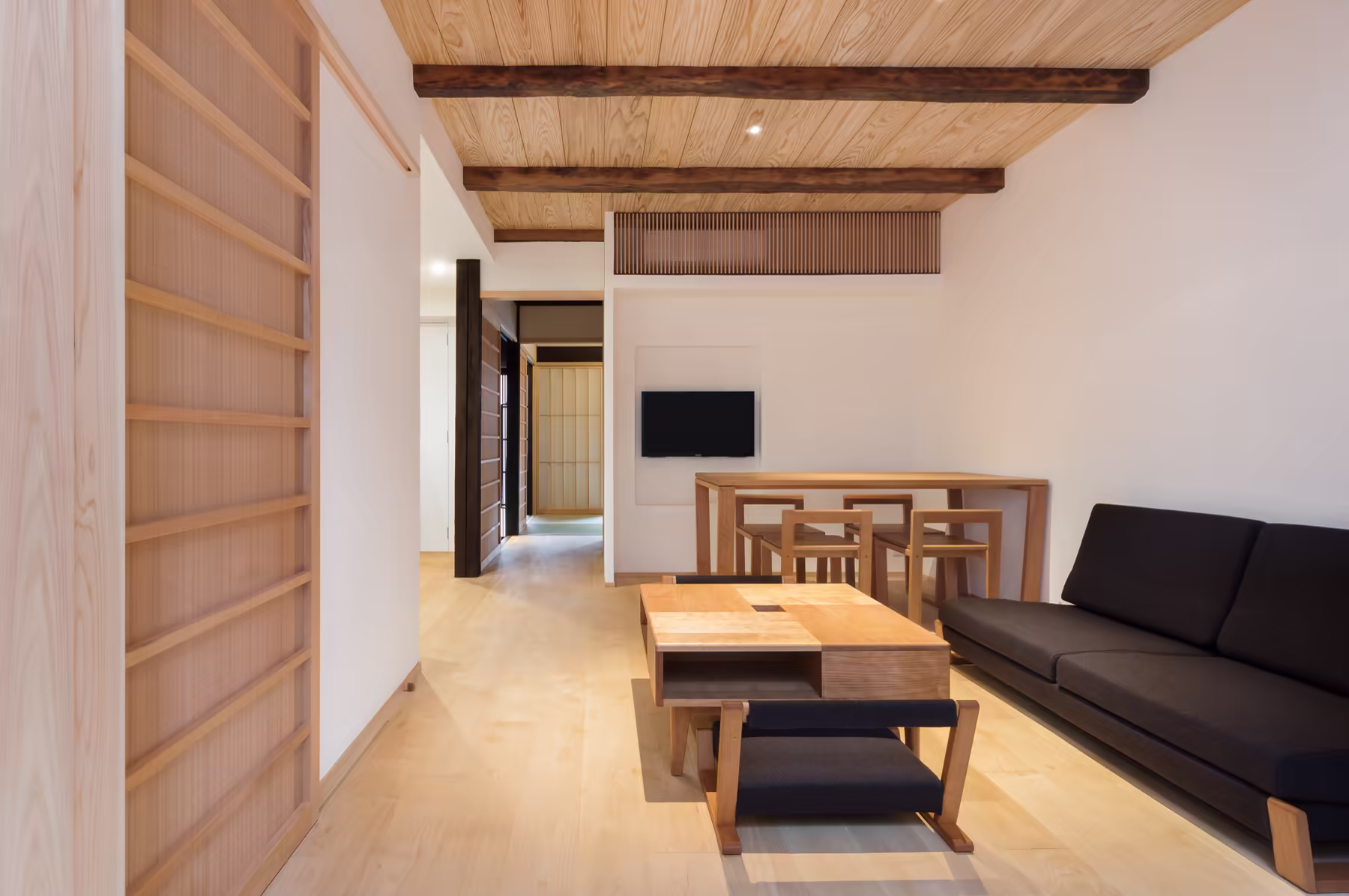 The living room end to end — low table, sofa and dining table under the exposed timber ceiling