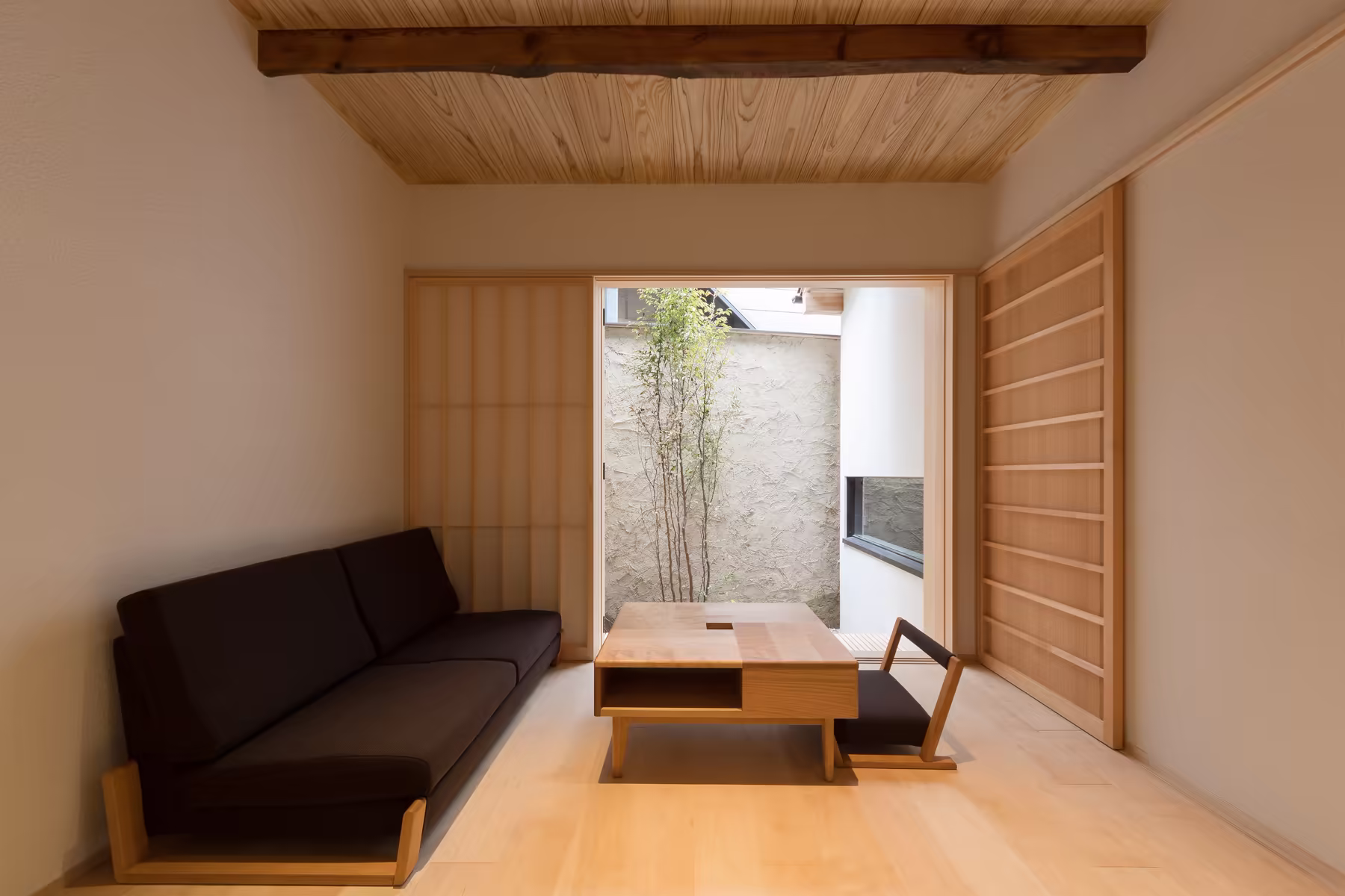 The lounge — a long dark sofa and low wooden table on pale timber, open to the planted courtyard